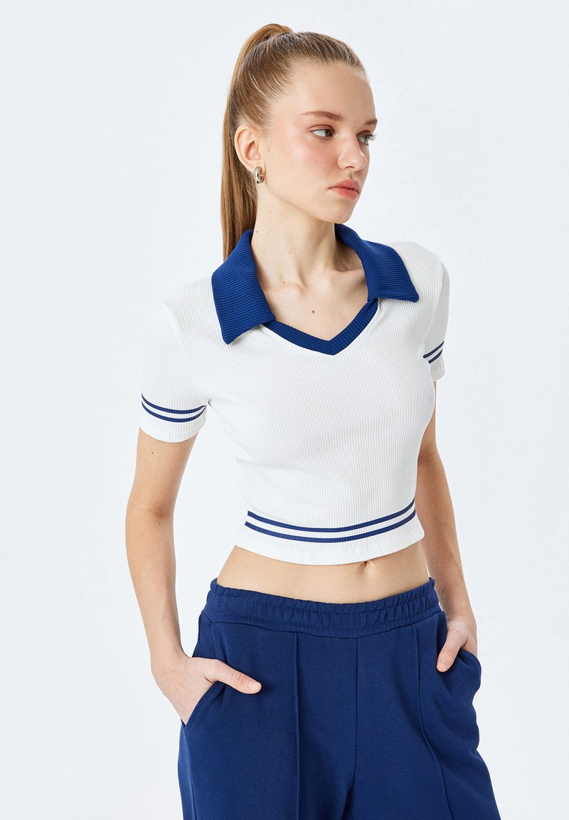 Vit ribbad kortärmad polo med marinblå krage och marinblå ränder vid fållen och ärmarna. Matchas med marinblå joggerbyxor.