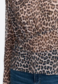 Leopard print top with long sleeves, featuring a gathered texture and gradual color transition from light beige to dark brown at the hem.