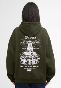 Λαδί φούτερ με μεγάλη λευκή εκτύπωση στην πλάτη, που απεικονίζει ένα φάρο και άλογα, φτιαγμένο από μαλακό υλικό.