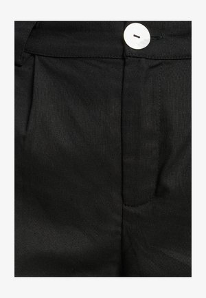 Melni auduma bikses ar gludu tekstūru, kurām ir plūstošs dizains, priekšējā krokas un balta pogu aizdare.