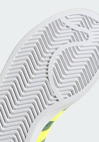 Suela de zapato con una base de goma blanca que presenta un patrón en zigzag y un acabado texturizado, rodeada de acentos verdes y amarillos en el material superior.