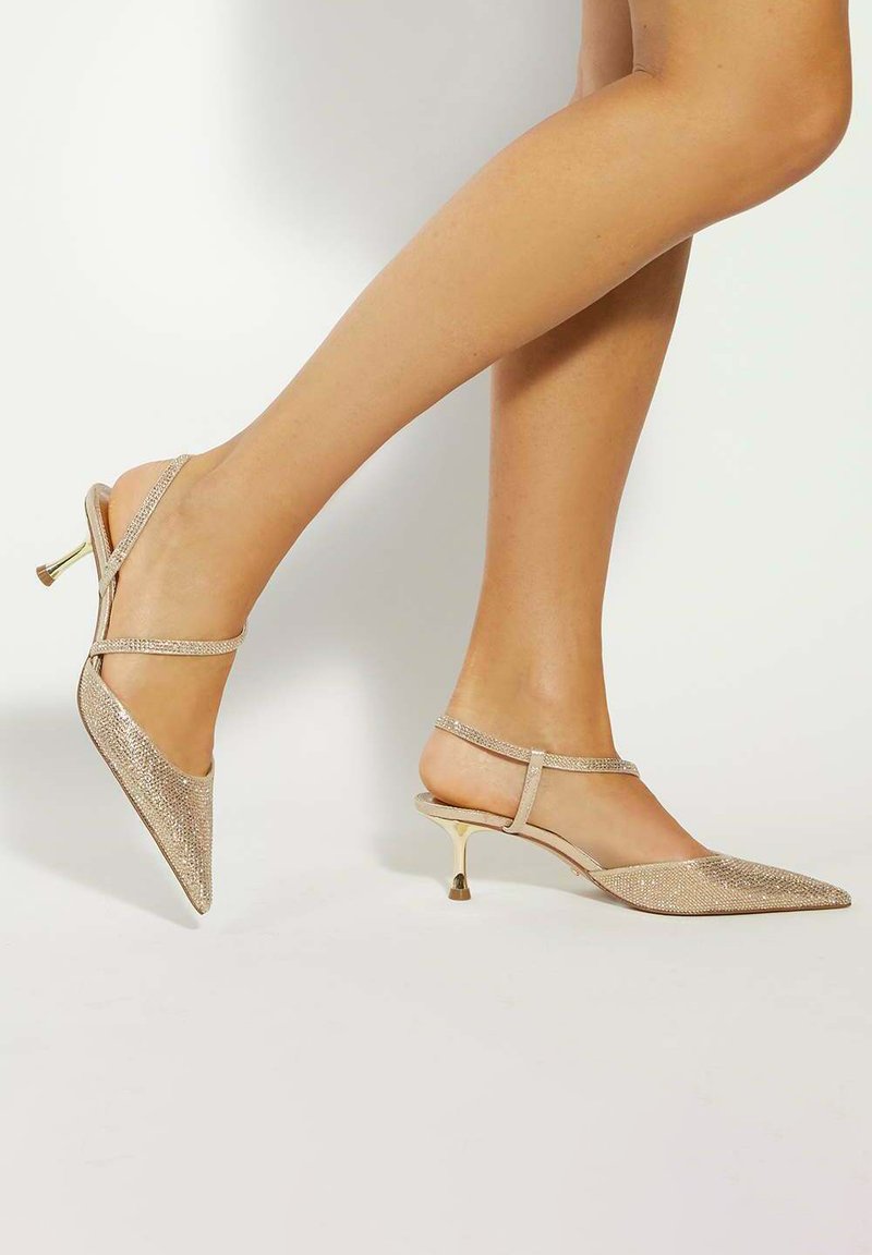 Sparkly beige slingback heels with a pointed toe. Features crisscross straps and a slender gold heel. Textured surface for added detail.
