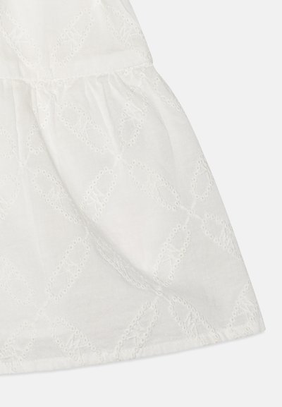 White cotton fabric featuring an eyelet embroidery pattern. The design includes a subtle scalloped edge at the hem. Soft texture.