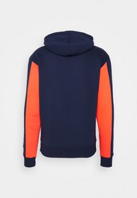 Felpa navy con pannelli laterali arancioni vivaci. Tessuto morbido, vestibilità rilassata, tasca a marsupio e cappuccio regolabile con coulisse. Polsini e orlo a coste.