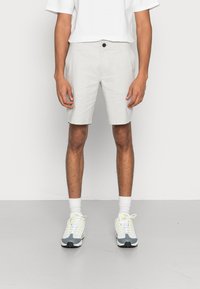 Lichtgrijze shorts gemaakt van een zachte stof, met een enkele knoop aan de voorkant, zijzakken en een getailleerde pasvorm. Draagt met een wit T-shirt en sneakers.