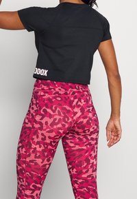 Zwart cropped t-shirt met een gladde textuur. Roze en rode legging met luipaardprint, gemaakt van een zacht, rekbaar materiaal met naden als detail.
