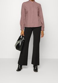 Rot-weiß kariertes Oberteil mit Puffärmeln, kombiniert mit schwarzen, ausgestellten Hosen und einer schwarzen, glänzenden Handtasche. Schwarze, hochhackige Stiefeletten.