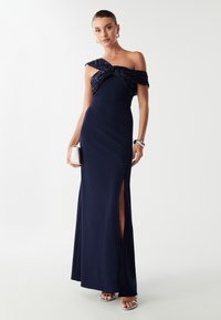 Granatowa sukienka z dopasowanym gorsetem i fasonem bez ramiączek, z fakturowanym, skręconym akcentem. Rozcięcie w spódnicy odsłania nogę.