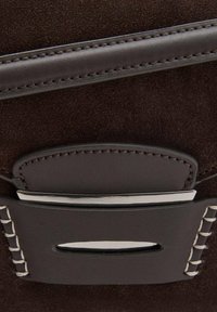 Sac à main en daim marron avec une bandoulière en cuir lisse, des accessoires en argent et des coutures contrastées le long du bord.