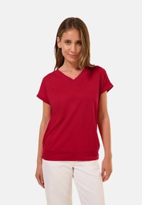 Blouse rouge à manches courtes en V, en matière douce avec une coupe décontractée et un ourlet froncé. Texture lisse et design simple.
