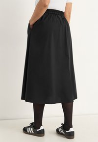 Black knee-length skirt with an elastic waistband, side pockets, and a smooth texture, paired with black tights and black sneakers.