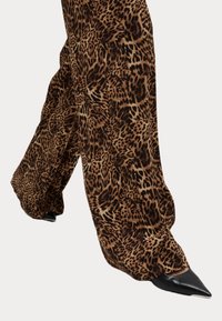 Leopardmönstrade vida byxor i brun och svart tyg med en jämn textur, kombinerat med spetsiga svarta skor.