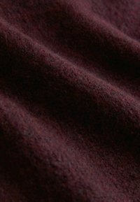 Burgundská vlněná tkanina s měkkým, texturovaným povrchem a různými odstíny, zobrazující jemná vlákna a jemný záhyb.