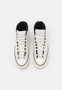 Höga sneakers med en krämfärgad ovandel, svart foder, vita snören och ett texturerat fleecepanel, med en gummitoecap och svarta detaljer.