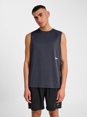 Ung mand med kort hår iført ærmeløs mørkegrå sportstrøje og sorte shorts, står mod en hvid baggrund.