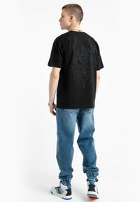 Czarna koszulka z krótkim rękawem z dużą, wyszukana szaro-skalną grafiką na plecach, w połączeniu z jasnoniebieskimi dżinsami i białymi trampkami.