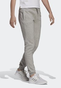 Grijze sweatpants van zacht materiaal, met een taps toelopend ontwerp, zijzakken en een tailleband met trekkoord. G gedragen met witte sneakers.