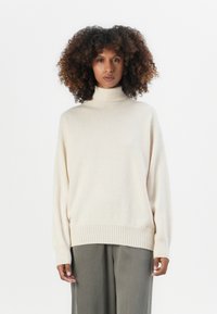 Cremfarbener Rollkragenpullover mit lockerer Passform, gerippten Bündchen und Saum. Weiche Textur, kombiniert mit hellgrauen weiten Hosen.
