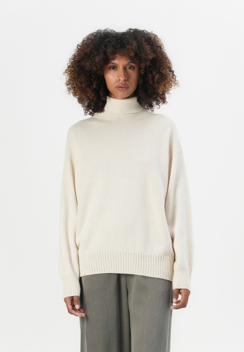 Cremfarbener Rollkragenpullover mit lockerer Passform, gerippten Bündchen und Saum. Weiche Textur, kombiniert mit hellgrauen weiten Hosen.