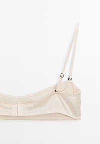 Beige bralette med justerbare stropper, glat tekstur og en hægte-lukning på bagsiden. Ingen polstring eller undertråd detaljer.
