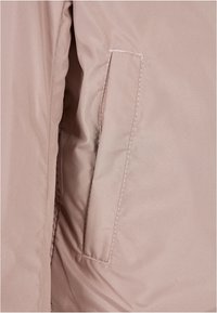Close-up of a light pink jacket pocket with visible stitching and part of a sleeve on the left side.