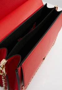 Sac à main en cuir rouge avec bandoulière chaîne dorée, ouverture supérieure dévoilant deux compartiments doublés de tissu noir et une poche intérieure.