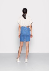 Rok denim biru dengan potongan mid-rise, kantong belakang, dan belahan di bagian bawah. Dipadukan dengan kemeja lengan pendek berwarna terang dan sepatu sneaker.