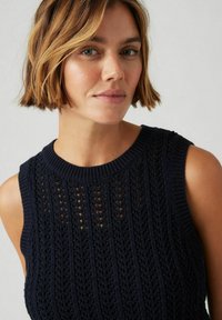 Stickad ärmlös topp i marinblått med ett strukturerat mönster som innehåller vertikala ränder och öppna vävda partier, rund hals och ribbad halsringning.