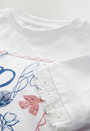 Weißes Baumwoll-T-Shirt mit floraler Stickerei in Blau und Pink, mit einer gewellten Spitzenkante am Ärmel.