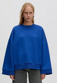 Übergroßer blauer Sweatshirt aus weichem Material, mit rundem Halsausschnitt, gesenkten Schultern und weiten Bündchen.