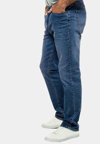 Blue denim jeans with a relaxed fit, featuring five pockets and visible stitching. Paired with white sneakers for contrast.