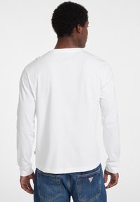 Hvid langærmet T-shirt med rund halsudskæring, glat tekstur og afslappet pasform, parret med blå denim jeans med et logo patch på baglommen.