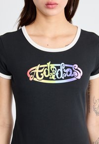 Sort tætsiddende t-shirt med en hvid ribbet rundhals, der har et farverigt, stiliseret "Adidas" logo i regnbuegradient på brystet.