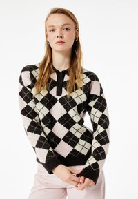 Sweter wykonany na drutach z wzorem argyle w kolorze czarnym, jasnoróżowym i miętowym. Posiada zapięcie na guziki przy kołnierzu oraz długie rękawy z ściągaczami.