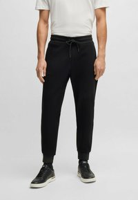 Svarta bomullsbyxor med elastisk midja och justerbar dragsko, nedtaperad bendesign och ribbade mudd, tillsammans med svarta sneakers.