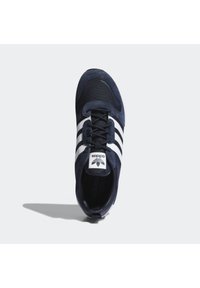 Marinblå sneaker med mesh och mockamaterial, med vita ränder och logotyp på tungan. Rundad tå och texturerade snören.