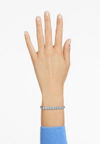 Blå ädelstensarmband på handleden, med en serie runda stenar som är infattade i silverfärgad metall, med en slät, polerad yta.