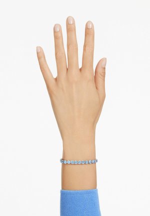 Blå ædelstensarmbånd på håndleddet, prydet med en række runde sten sat i sølvfarvet metal med en glat, poleret overflade.