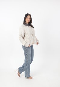 Texturerad beige cardigan med tre stora knappar och sidfickor, kombinerad med ljusblå höga jeans och sandaler med genomskinlig klack.