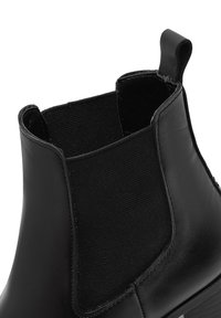 Botín Chelsea negro con material de cuero suave, paneles laterales elásticos y una lengüeta para facilitar el calzado. Diseño de punta redonda y suela plana.