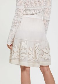 Biała spódnica haftowana, z warstwowym wykonaniem, przejrzystym materiałem i teksturowanymi akcentami wzdłuż hemu oraz na wzorach.