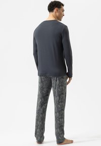 Heren pyjama set bevat een donkergrijze lange mouw top en een patroon, losse broek in marineblauw met een paisley ontwerp. Zachte stoftextuur.