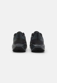 Black athletic shoes with a mesh upper, textured detailing, visible cushioning, and a rugged outsole. Features Gore-Tex branding on the sides.