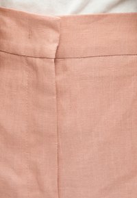 Gros plan d’un tissu en lin rose montrant une ceinture avec une fermeture éclair latérale cachée et des détails de couture soignés.