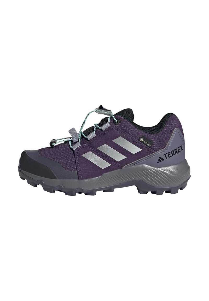 Chaussure de randonnée violette avec un dessus en maille, un capuchon de protection en caoutchouc gris et des bandes réfléchissantes argentées. Dispose d'un système de lacets sécurisé et d'une semelle texturée.