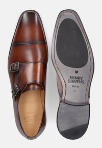 Braune Lederschuhe mit einem Doppel-Monk-Riemendesign, glatter Textur, abgerundeter Zehenform und einer Sohle mit Gummielementen und geprägtem Branding.