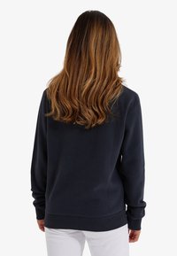 Marinblå hoodie tillverkad av mjukt tyg, med långa ärmar, ribbad avslutning och en avslappnad passform. Inga synliga mönster eller detaljer.