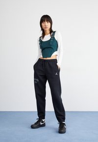 Grön randig cropped topp med silverdetaljer, tillsammans med svarta joggers med en vit logotyp, och svarta sneakers med vita accenter.