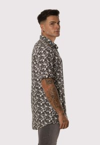 Camisa de manga corta en blanco y negro con un patrón repetido de calaveras y flores, cuello abotonado y corte relajado.