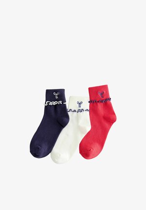 Tri gležnjače u mornarsko plavoj, bijeloj i crvenoj boji s naboranim rubovima i malim izvezenim mašnicama iznad nabora na bijeloj pozadini.